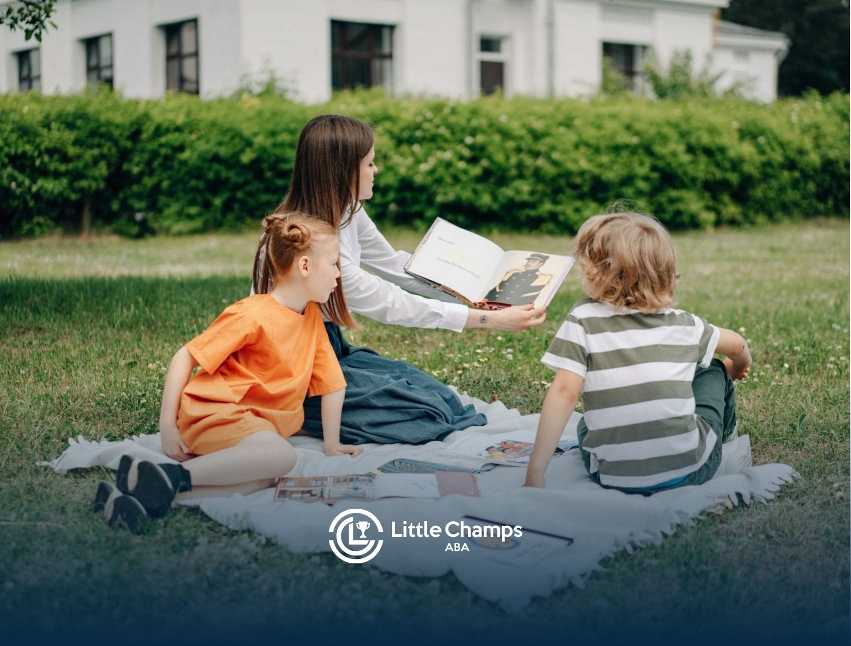 An ABA therapist reading a book to two autistic children sitting outside on a blanket in Colorado.