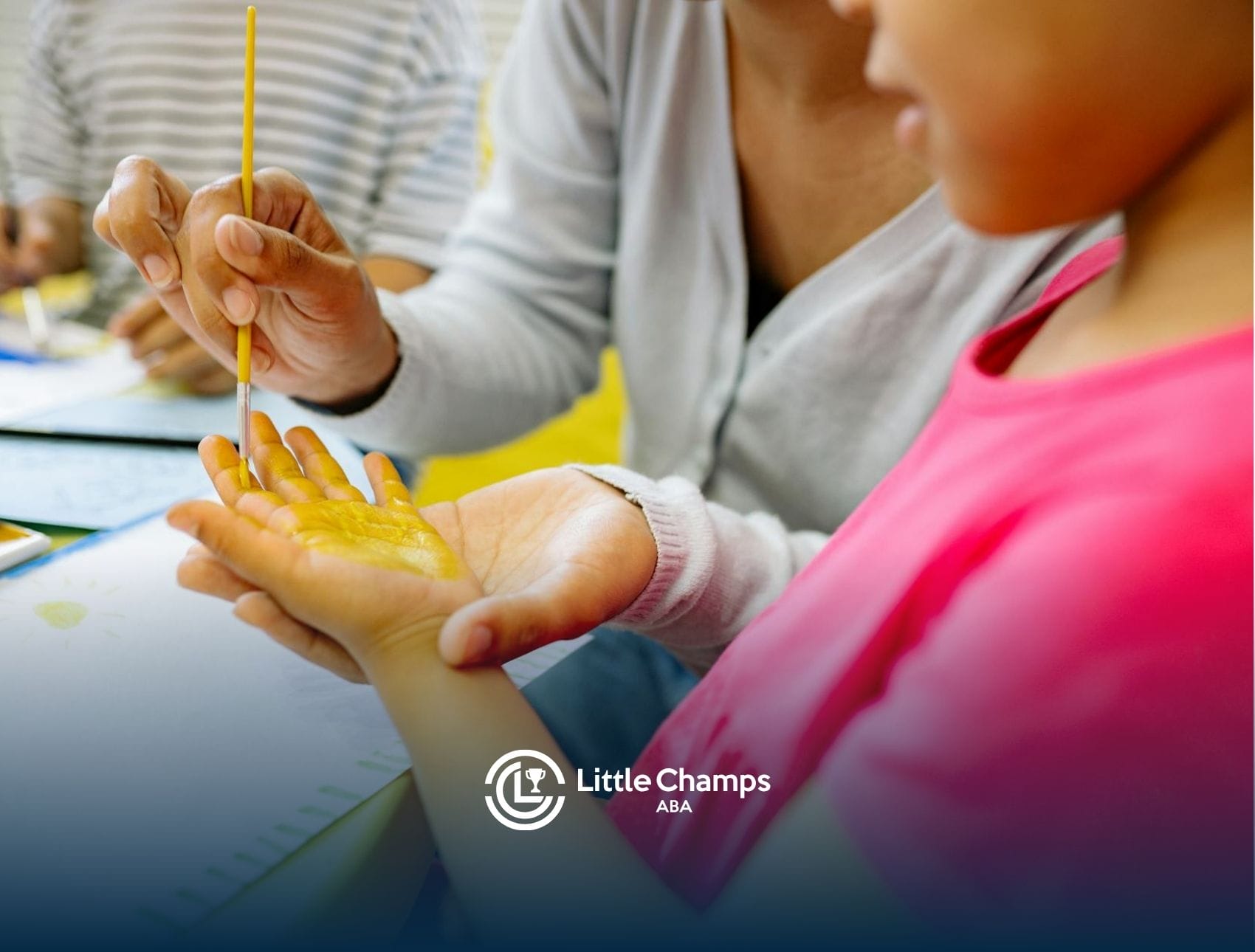 ABA therapist painting autistic child’s hand with yellow paint during school-based ABA therapy in CO.