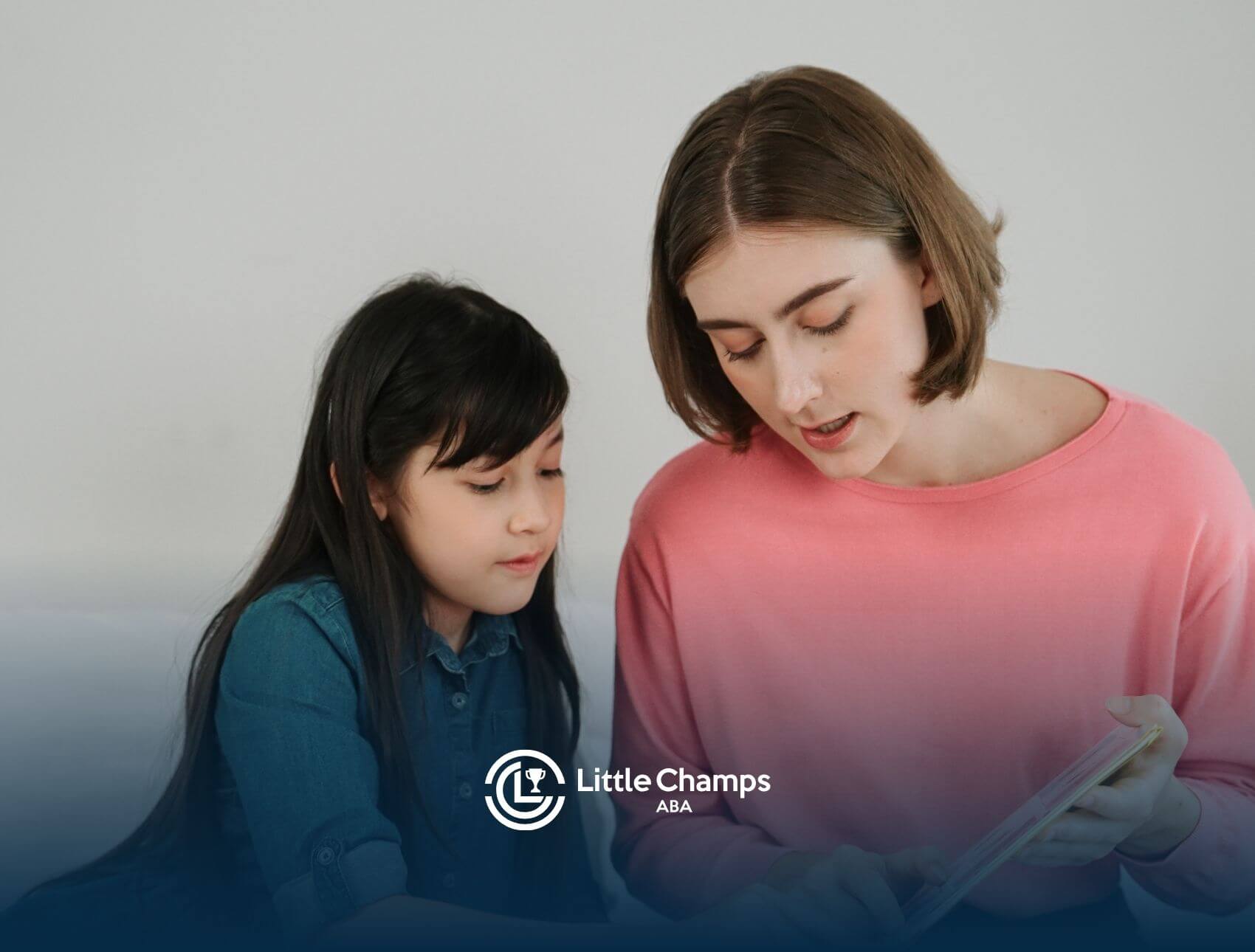 A BCBA reading or explaining something to a young girl while sitting together in ABA therapy.