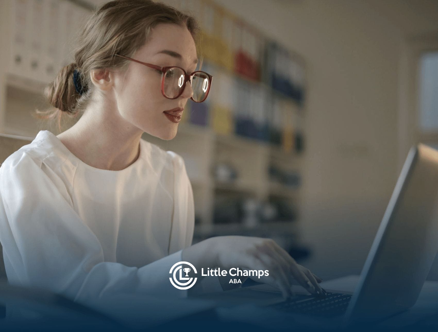 A BCBA student with red glasses studying on a laptop for BCBA exam in a study room with shelves and folders behind.