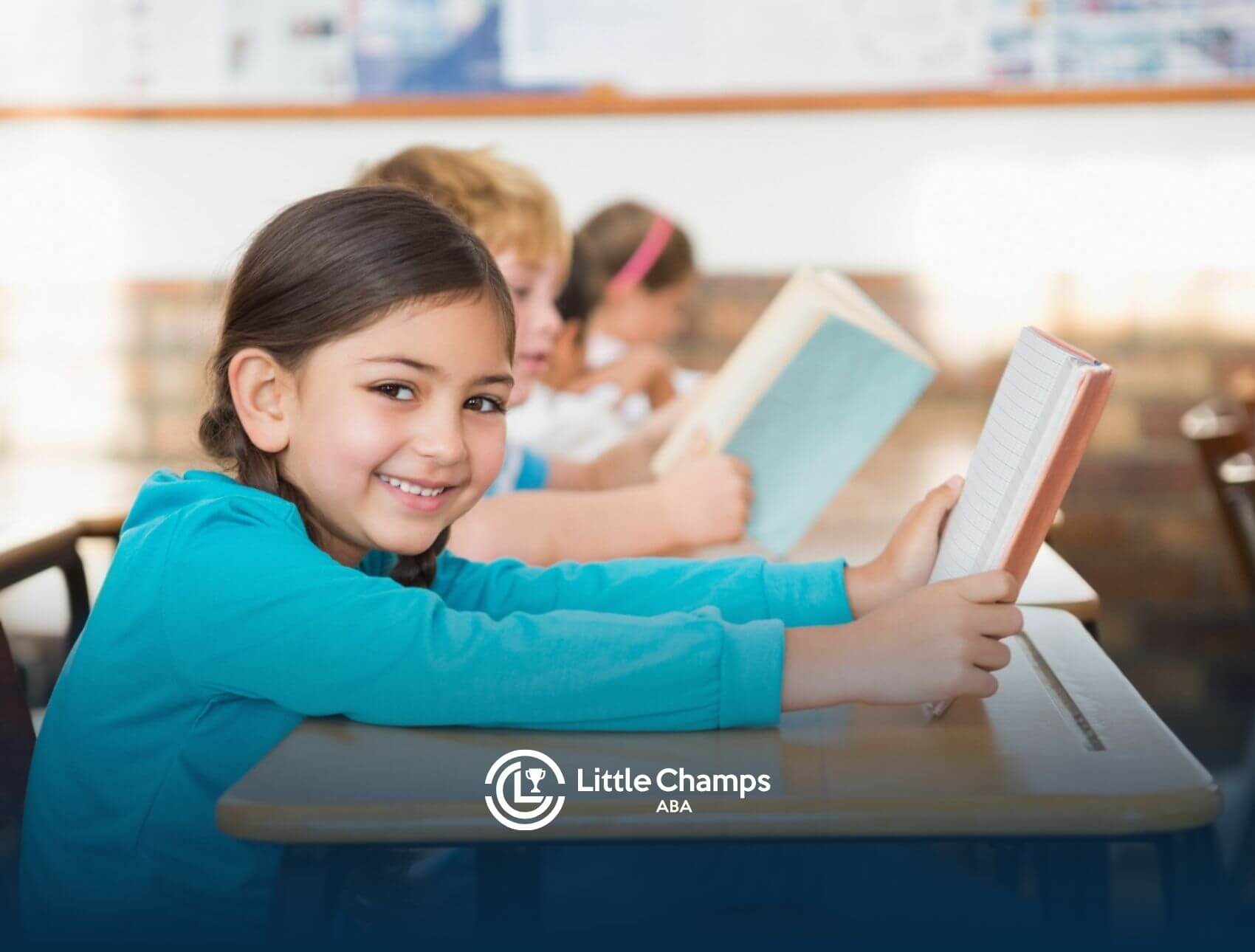 A girl with autism smiling while holding a book in a classroom.
