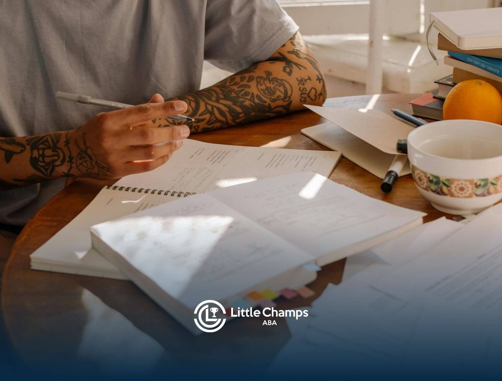 Tattooed ABA student studying at a table with open notebooks, papers, and coffee in Virginia.