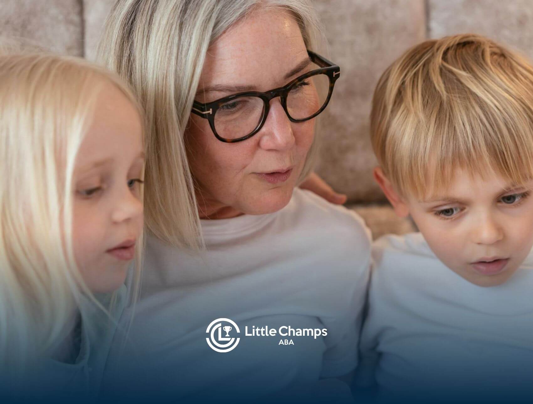 ABA therapist reading with two autistic children sitting closely beside her while looking down.