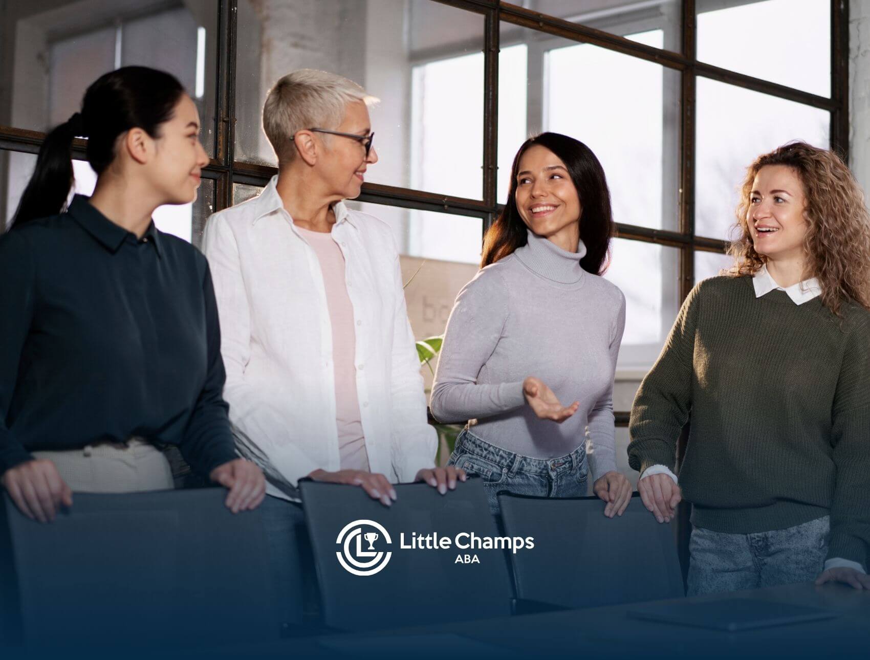 A group of four women ABA therapist in a meeting discussing work while standing and smiling at each other.